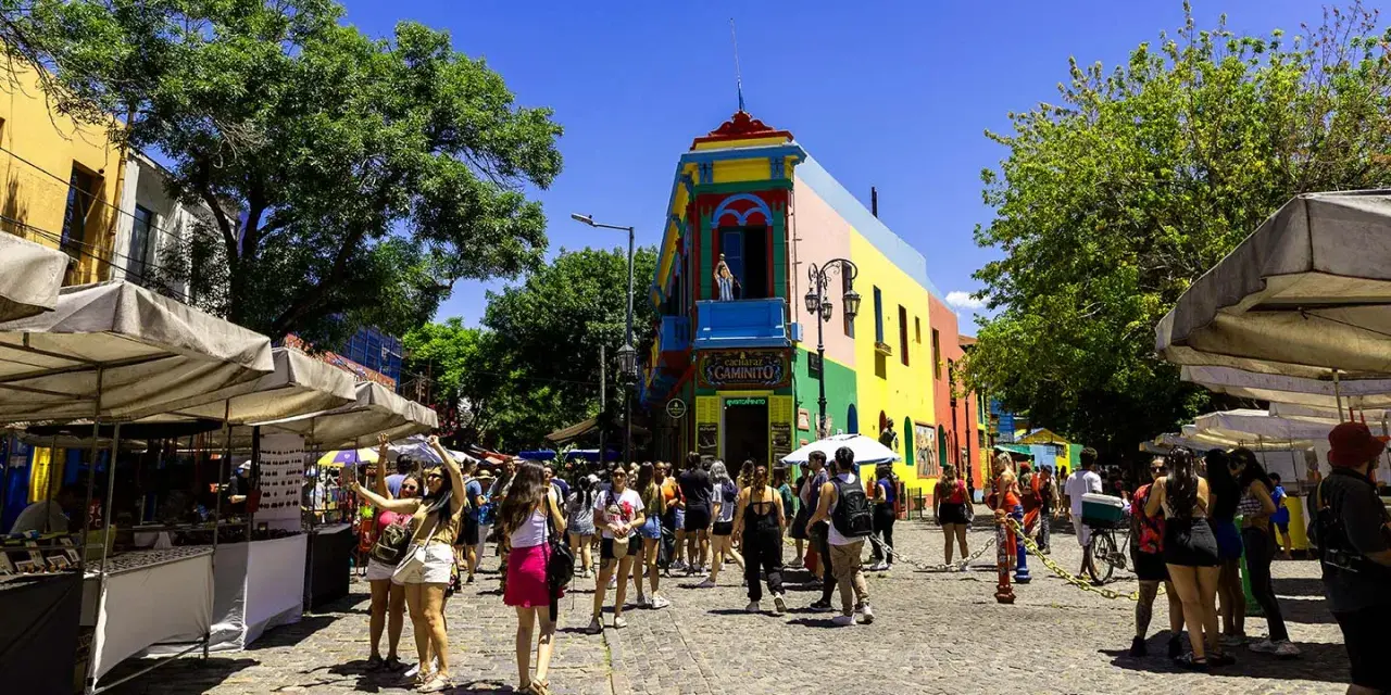 Färgglada hus och marknadsstånd i Buenos Aires. En livlig gata med människor som njuter av solen.