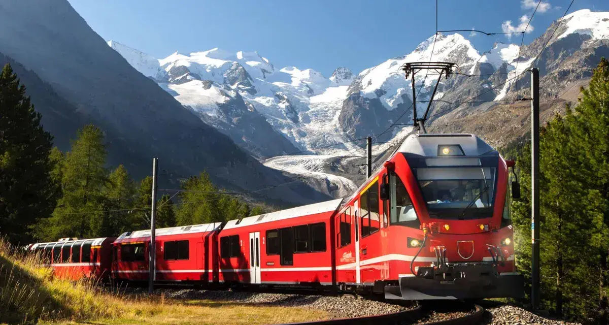 Ett rött tåg slingrar sig fram genom ett dramatiskt alplandskap med snöklädda berg. Kanske är det ett tåg till Italien, med hisnande vyer längs vägen.