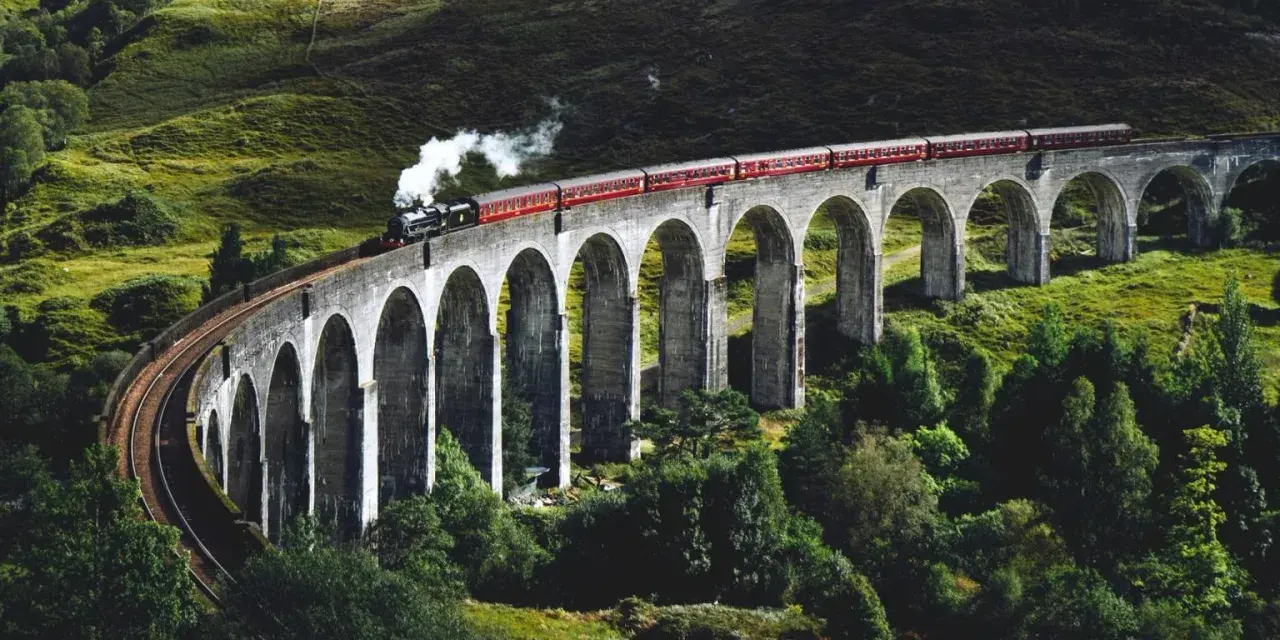Ångloket på Glenfinnanviadukten i Skottland, som påminner om Harry Potter tåg skottland, ångar fram över den gröna dalen.