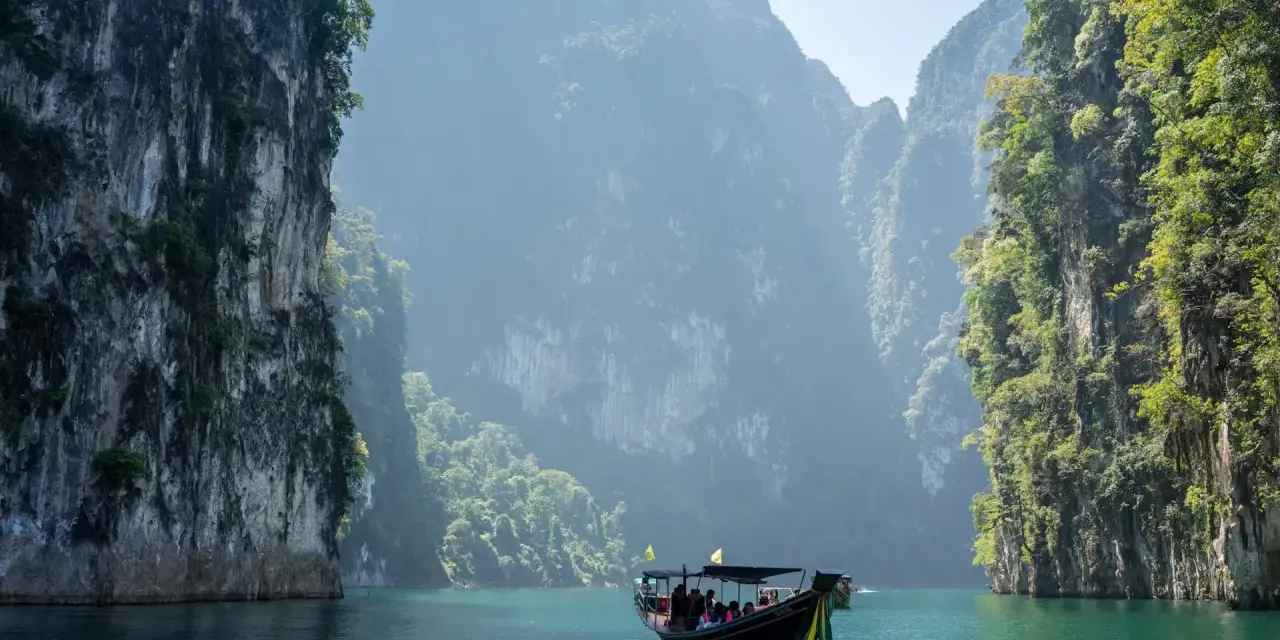 En båt färdas på turkost vatten genom dramatiska kalkstensklippor i Khao Sok nationalpark.