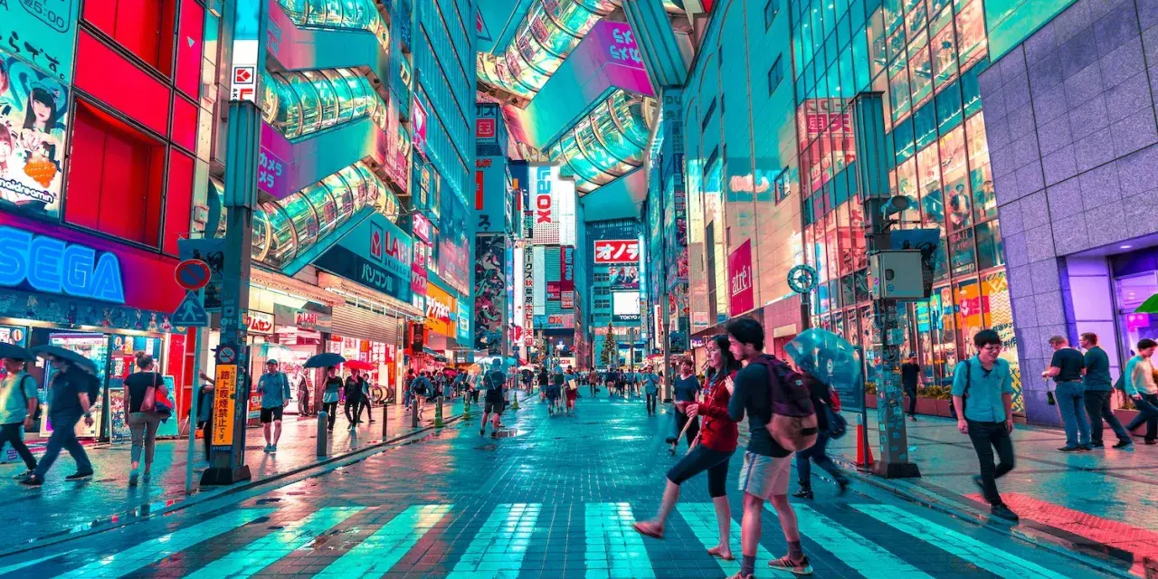 Neonbelyst gata i Tokyo, perfekt för din tokyo reseguide. Människor promenerar under paraplyer i regnet bland blinkande skyltar.