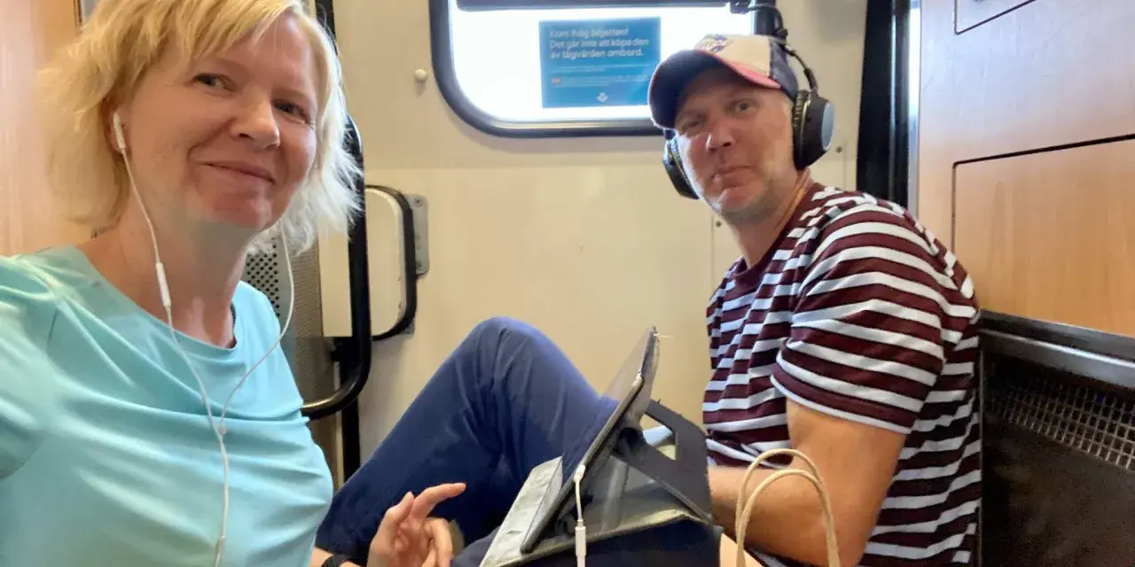 Ett par på tåget, redo för en resa. Kanske är det ett tåg till Grekland, med hörlurar och surfplatta för underhållning.