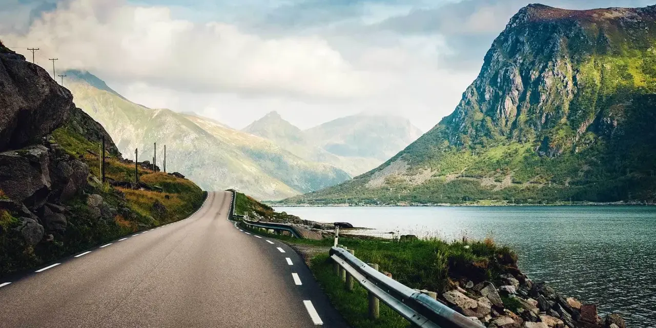 Väg som slingrar sig genom dramatiskt landskap med berg och fjord. En drömresa till Lofoten från Stockholm.