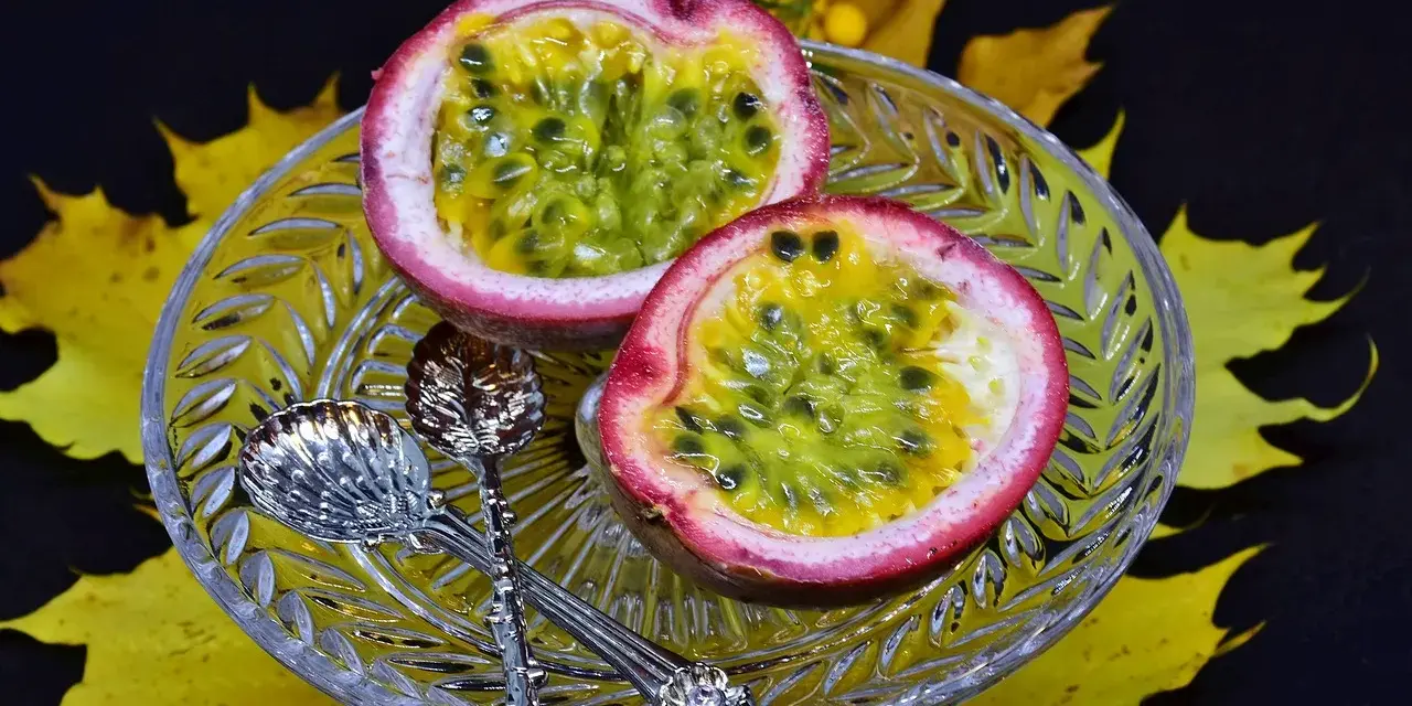 Två halvor av passionsfrukt på en kristallskål, omgivna av höstlöv. Dessa exotiska frukter ser läckra ut!