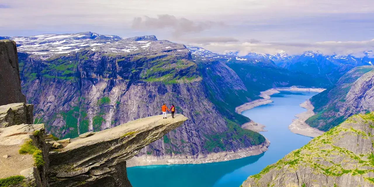 Två personer står på Trolltunga, en klippavsats i Norge, med en fantastisk utsikt över bergen och naturen.