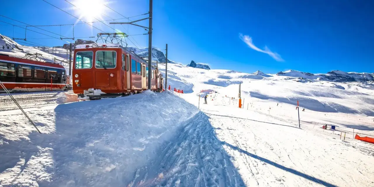 Ett snötäckt tåg i Schweiz, redo att transportera skidåkare uppför berget under en strålande solig dag.
