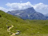 Vandrare på en stig i Dolomiterna, omgiven av gröna sluttningar och majestätiska berg under en molnig himmel.
