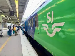 Folk väntar på perrongen vid vagnhall B. Ett grönt SJ-tåg står redo för resan, kanske till och med ett tåg till London.