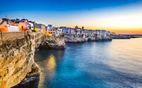 Solnedgång över Polignano a Mare, en pittoresk kuststad i Puglia, Italien. Vita hus klättrar på klipporna ovanför det turkosblå havet.