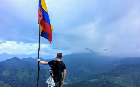 Vandrare med Colombias flagga på en bergstopp. Trots ryktet om att en resa till Colombia kan vara farligt, njuter han av den dramatiska utsikten.