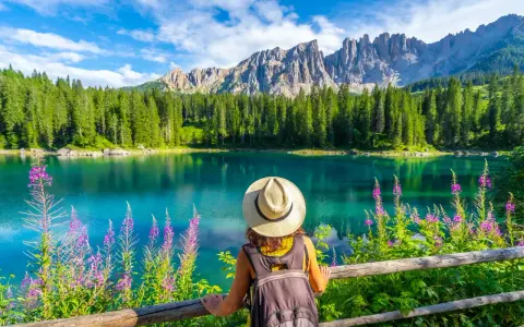 En kvinna med hatt och ryggsäck njuter av en vacker sommardag vid en turkos sjö i Dolomiterna.