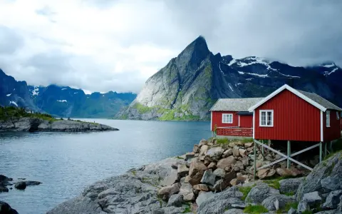 Två röda stugor vid en sjö i Norge, med dramatiska berg i bakgrunden. Perfekt för den som vill vandra i Norge.