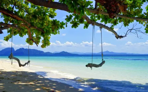 Gungor hänger från ett träd vid en strand i Thailand. Vackert turkost vatten och berg i bakgrunden. En idyllisk plats, trots att det är regnperiod.