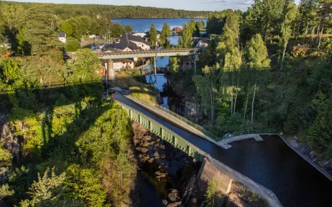 Vattenvägar och akvedukter i Sverige, med gröna broar som leder vatten över en ravin, omgivna av frodig skog och en sjö i bakgrunden.