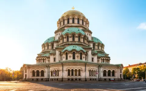 Imponerande kyrka med gröna kupoler och ett gyllene kors i Sofia, Bulgarien. En vacker syn i morgonsolen.