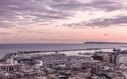 En vacker solnedgång över hamnen i Alicante i december. Molnen färgas i rosa och lila över havet och staden.