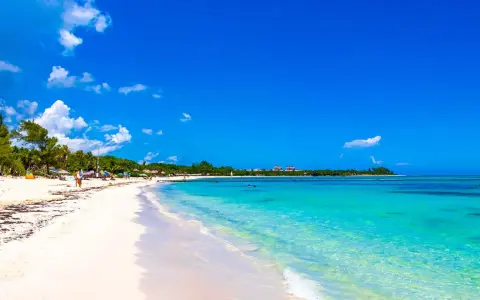 Vacker strand med turkost vatten och vita moln. Trots den idylliska vyn, kan Playa del Carmen vara farligt.