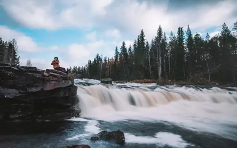 Person sitter på en klippa vid ett forsande vattenfall i Dalarna, ett perfekt utflyktsmål.