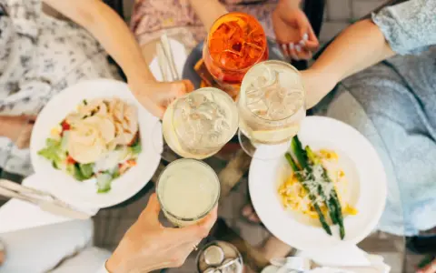 Vänner skålar med drinkar och njuter av en härlig milano mat-upplevelse med sallad och pasta med sparris.