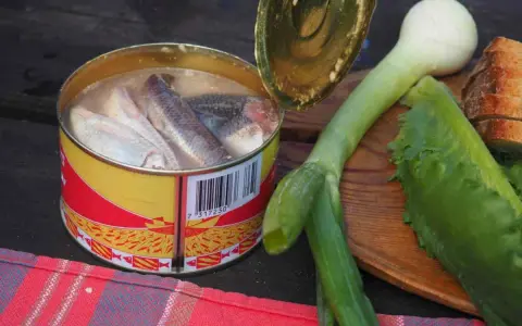 En burk med sill, en klassisk del av **comida tipica sueca**, ligger bredvid färska grönsaker och bröd.