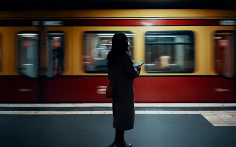 Kvinna med mobil på perrongen i Berlin, en gul och röd tunnelbanevagn susar förbi. Perfekt för din berlin reseguide.