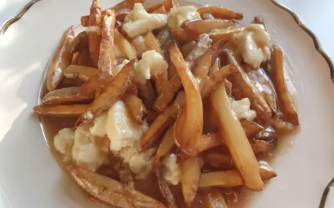 En tallrik med kanadas nationalrätt, poutine: friterade pommes frites, ostbitar och sås.