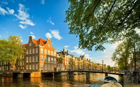 En vacker kanalvy i Amsterdam med klassiska hus, broar och båtar. Perfekt för din amsterdam reseguide.