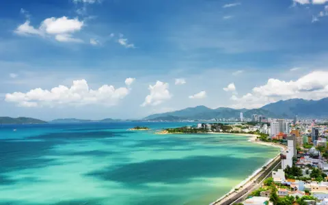 Vacker vy över Nha Trang, Vietnam, med turkost vatten, gröna kullar och en stad vid kusten under en blå himmel med moln.