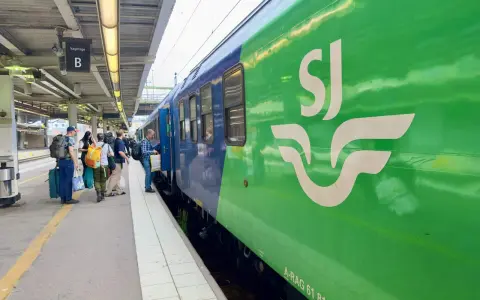 Folk väntar på perrongen vid vagnhall B. Ett grönt SJ-tåg står redo för resan, kanske till och med ett tåg till London.