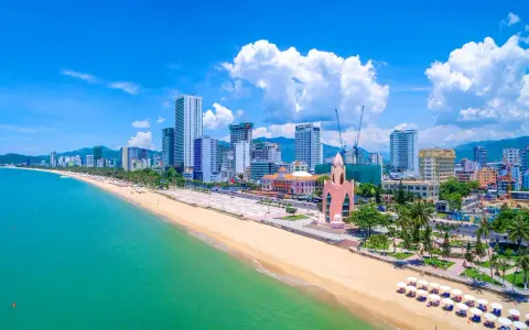 En vidsträckt strand med turkost vatten och en stadssilhuett i bakgrunden. Nha Trang beach är en populär destination.