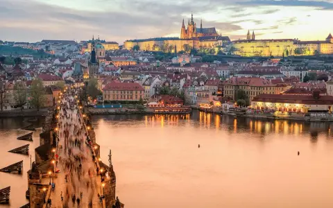 En livlig kväll på Karlsbron i Prag, med tusentals besökare som promenerar mot slottet. En perfekt vy för den som tar tåg till Prag.