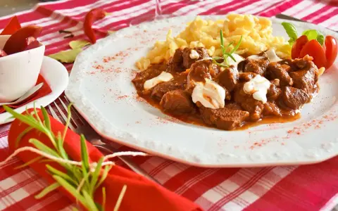 En smak av mat i Budapest: mustig gulasch med nokedli, garnerad med gräddfil och en rosmarinkvist. En röd chili och en tomatblomma fulländar upplägget.
