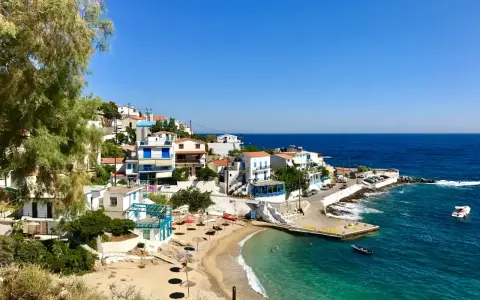 En pittoresk kustby på Ikaria, Grekland, med vita hus, en sandstrand och turkost vatten.