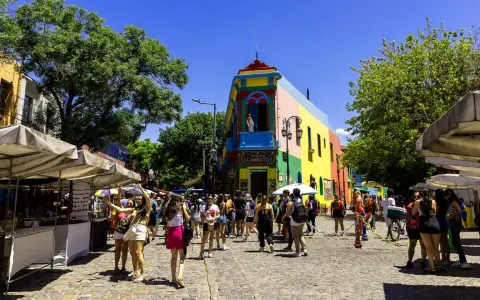 Färgglada hus och marknadsstånd i Buenos Aires. En livlig gata med människor som njuter av solen.