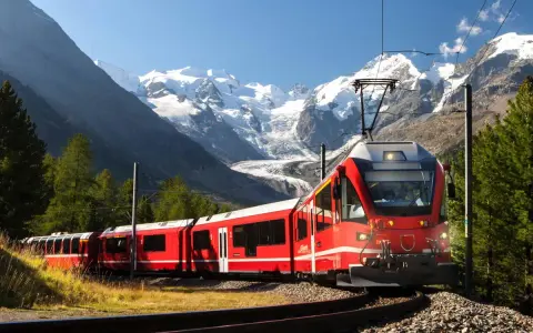 Ett rött tåg slingrar sig fram genom ett dramatiskt alplandskap med snöklädda berg. Kanske är det ett tåg till Italien, med hisnande vyer längs vägen.