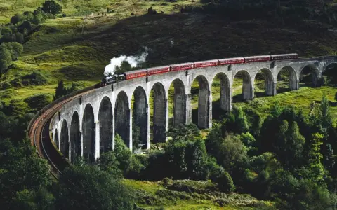 Ångloket på Glenfinnanviadukten i Skottland, som påminner om Harry Potter tåg skottland, ångar fram över den gröna dalen.