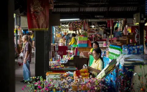 En livlig marknad i Bangkok med försäljare och kunder bland färgglada varor och blommor.