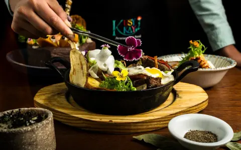 En hand dekorerar en mustig gryta med kött, potatis och blommor. En utsökt rätt som påminner om kanadensiskt kök.