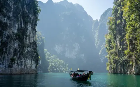 En båt färdas på turkost vatten genom dramatiska kalkstensklippor i Khao Sok nationalpark.
