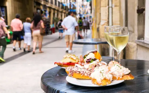 Njut av utsökt san sebastian mat och vitt vin på ett café. Folk promenerar på gatan i bakgrunden.