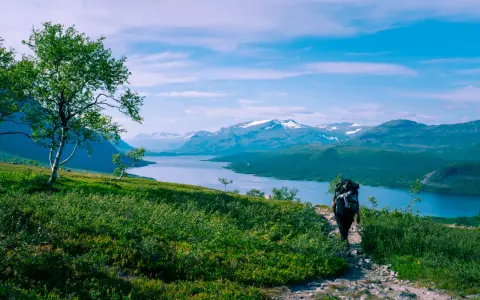 Vandrare med stor ryggsäck på en stenstig, njuter av storslagna vyer över sjö och snöklädda berg. Perfekt för vandringsleder Norrland.