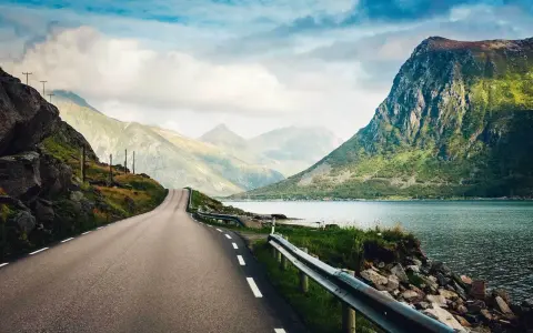 Väg som slingrar sig genom dramatiskt landskap med berg och fjord. En drömresa till Lofoten från Stockholm.