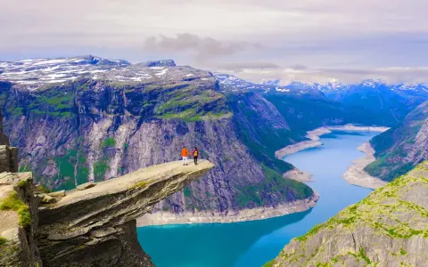 Två personer står på Trolltunga, en klippavsats i Norge, med en fantastisk utsikt över bergen och naturen.