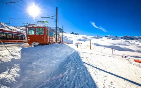 Ett snötäckt tåg i Schweiz, redo att transportera skidåkare uppför berget under en strålande solig dag.
