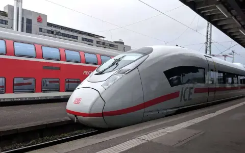 Ett modernt ICE-tåg står redo vid perrongen, perfekt för en resa med tåg till Tyskland. Bredvid syns ett rött dubbeldäckartåg.