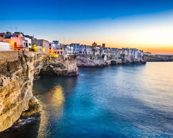 Solnedgång över Polignano a Mare, en pittoresk kuststad i Puglia, Italien. Vita hus klättrar på klipporna ovanför det turkosblå havet.