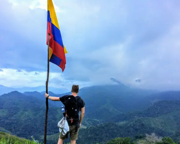 Vandrare med Colombias flagga på en bergstopp. Trots ryktet om att en resa till Colombia kan vara farligt, njuter han av den dramatiska utsikten.