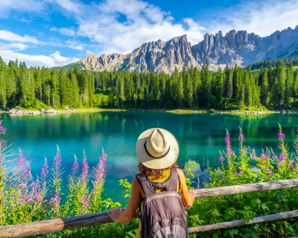 En kvinna med hatt och ryggsäck njuter av en vacker sommardag vid en turkos sjö i Dolomiterna.