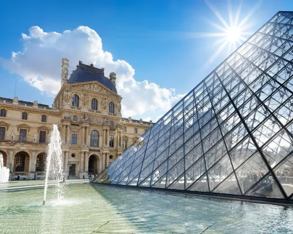 Louvren, ett berömt konstmuseum i Paris, med sin ikoniska glaspyramid och fontäner i förgrunden under en solig himmel.
