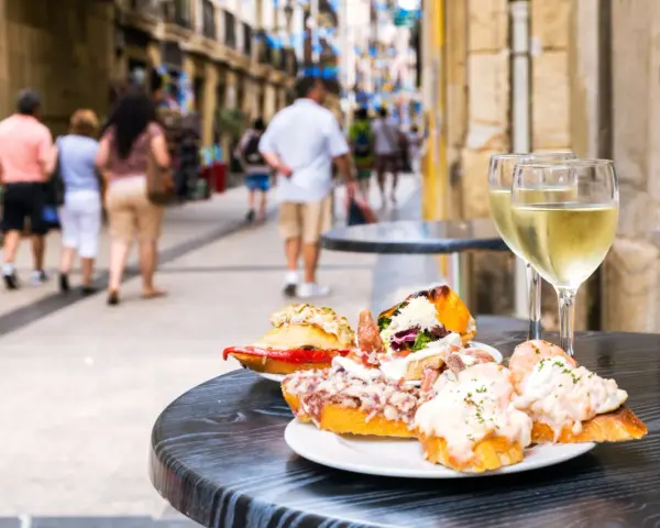 Tapas och vin på en uteservering i San Sebastián. Folk promenerar förbi på den livliga gatan.